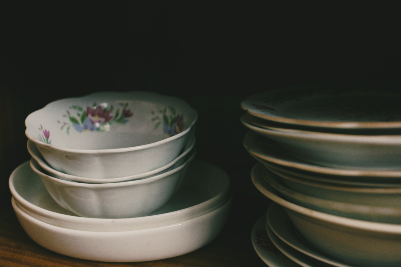 Services A close-up of floral bowls and dishes stacked inside a dark cupboard.